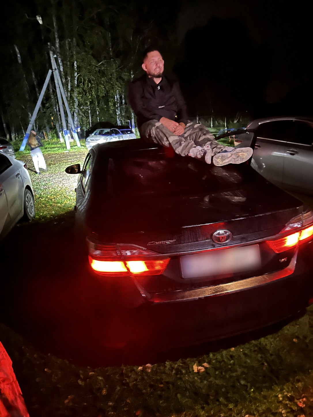 Никитос сидит на крыше чёрной Toyota в свете красных задних фонарей